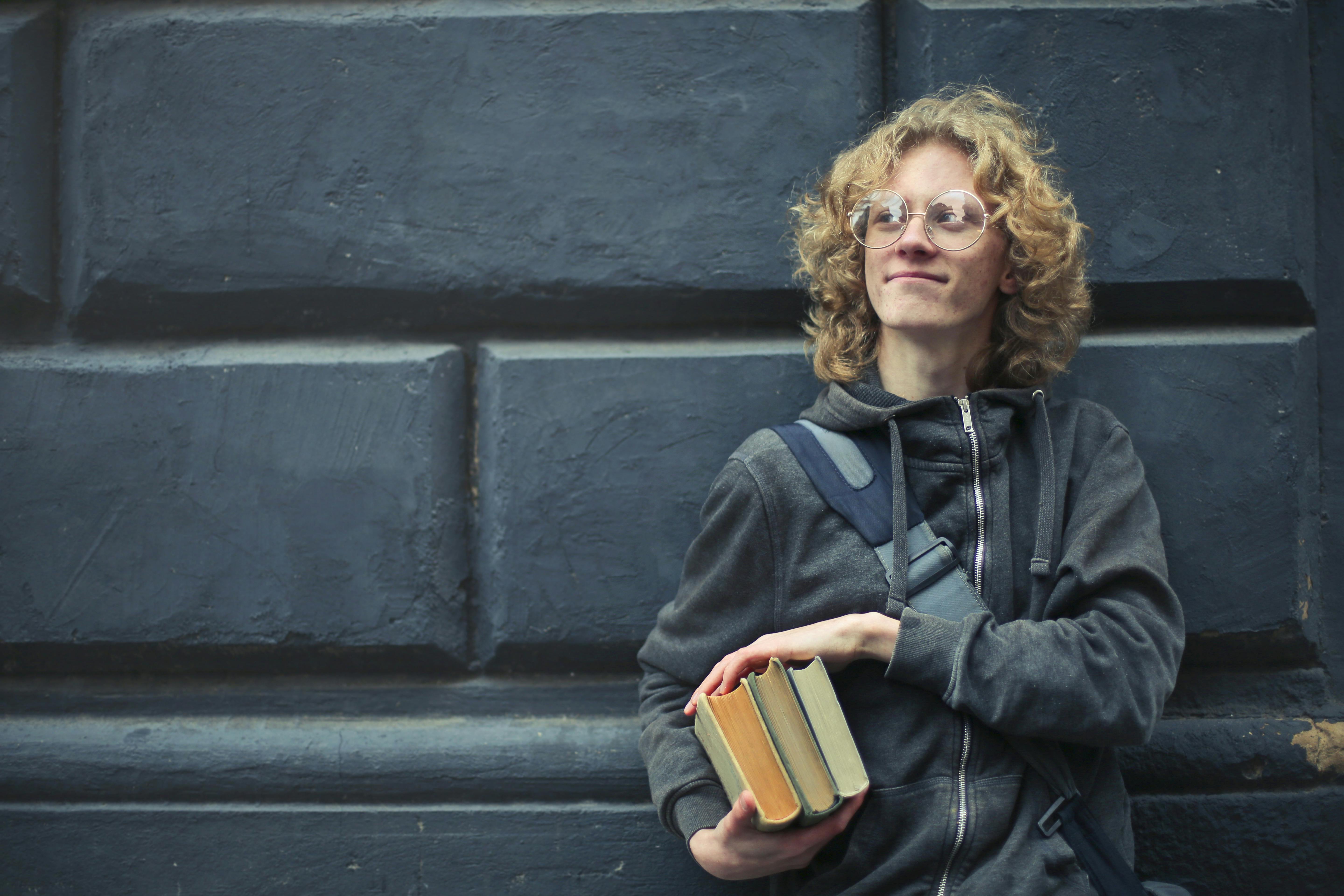 Boy stands next to a wall holding a book