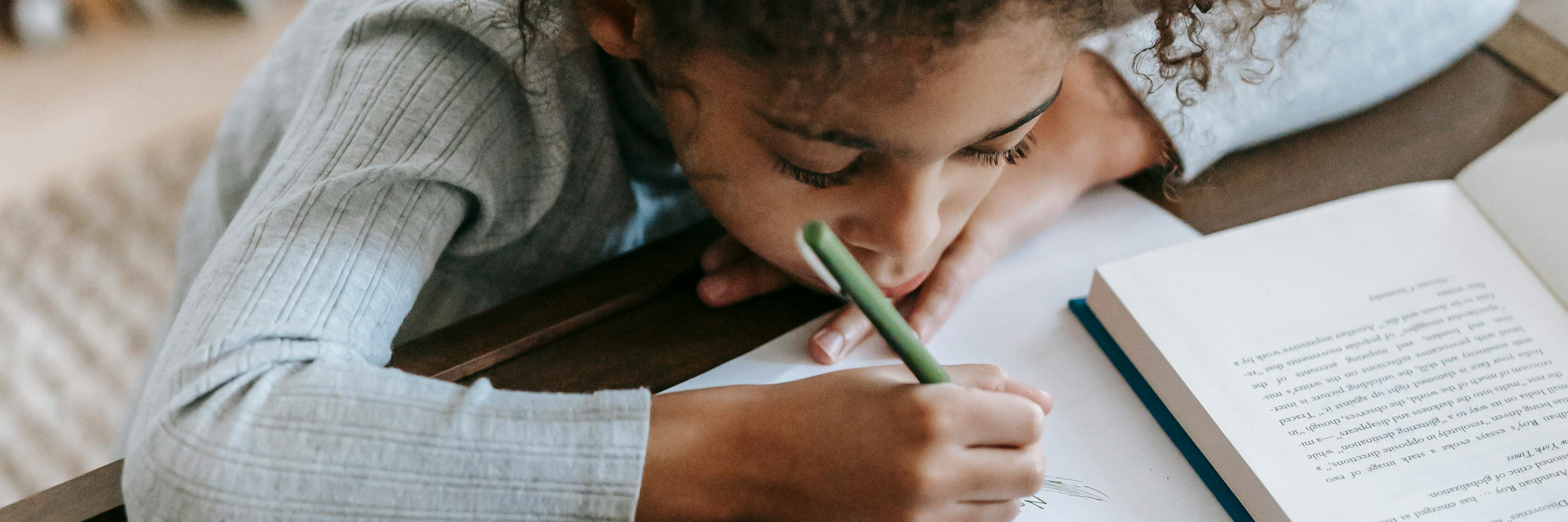 Child holding book with a pencil looking considerative